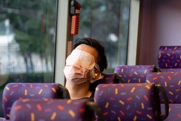 A masked passenger sleeps on board a "quiet bus" with the aid of an eye shield and ear plugs.