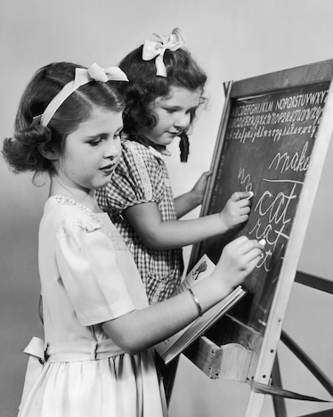 two girls practice cursive on a blackboard