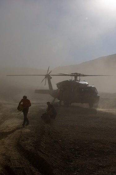 Rescue team members carry equipment from a helicopter, the air full of dust.