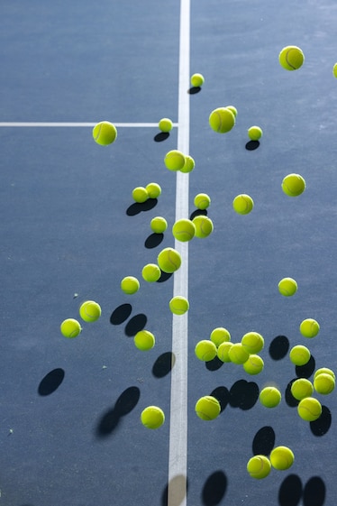 Tennis balls flying over white line on the blue tennis court surface.