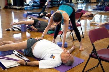 A yoga instructor helps a student to stretch in a yoga class.
