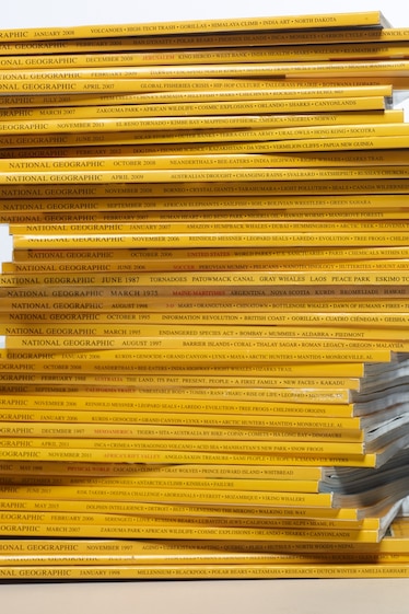 Stacks of past issues of National Geographic Magazine against a white background.