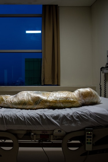 human body wrapped in plastic on hospital bed.