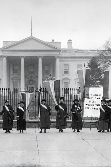women standing in front of the white house holding banners