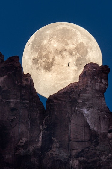 a person walking between two peaks on a slackline in front of the moon